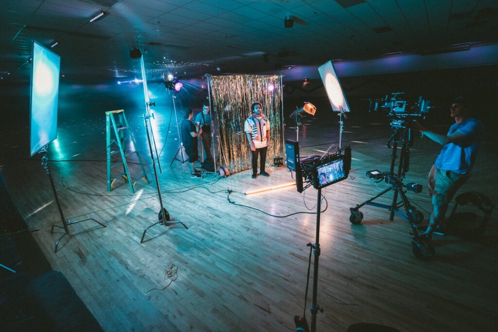 man standing in front of cameras with string lights background shooting video advertising